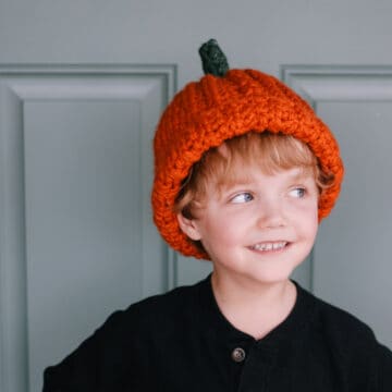 A child wearing a ribbed pumpkin hat, looking mischievously to the left.
