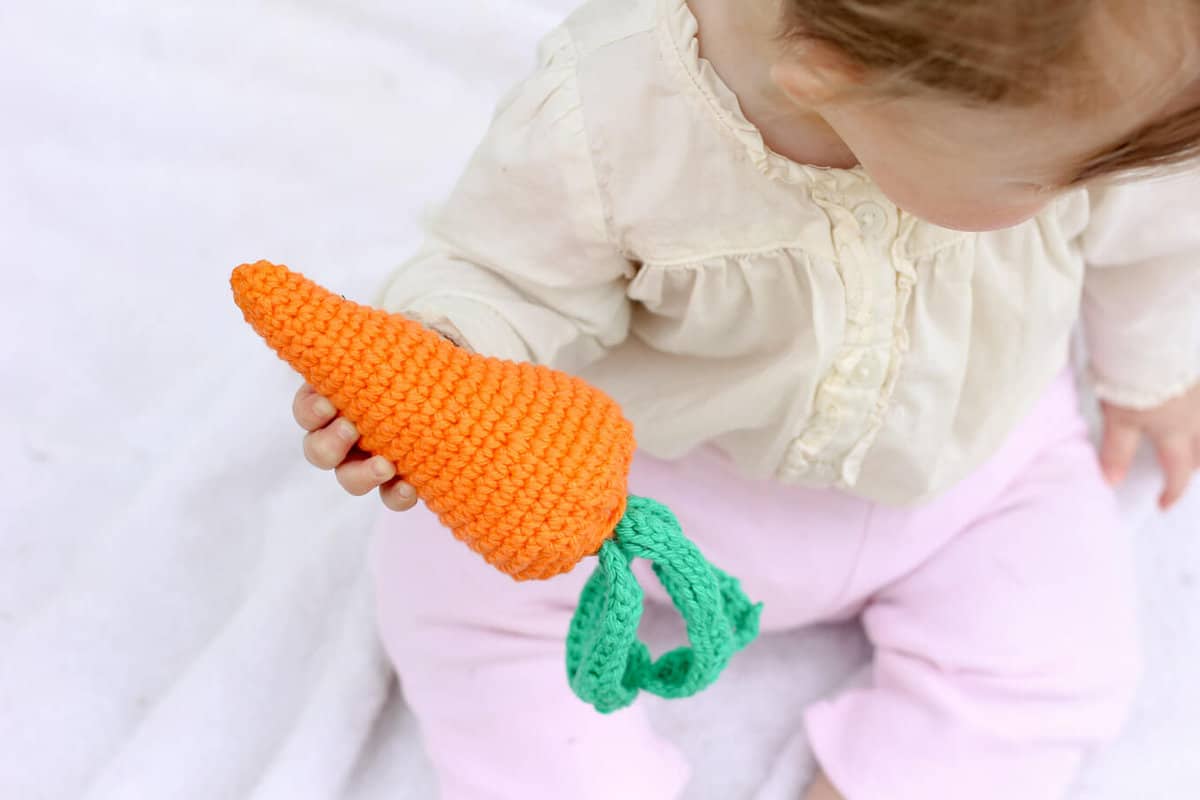 Baby holding an amigurumi crochet carrot rattle.