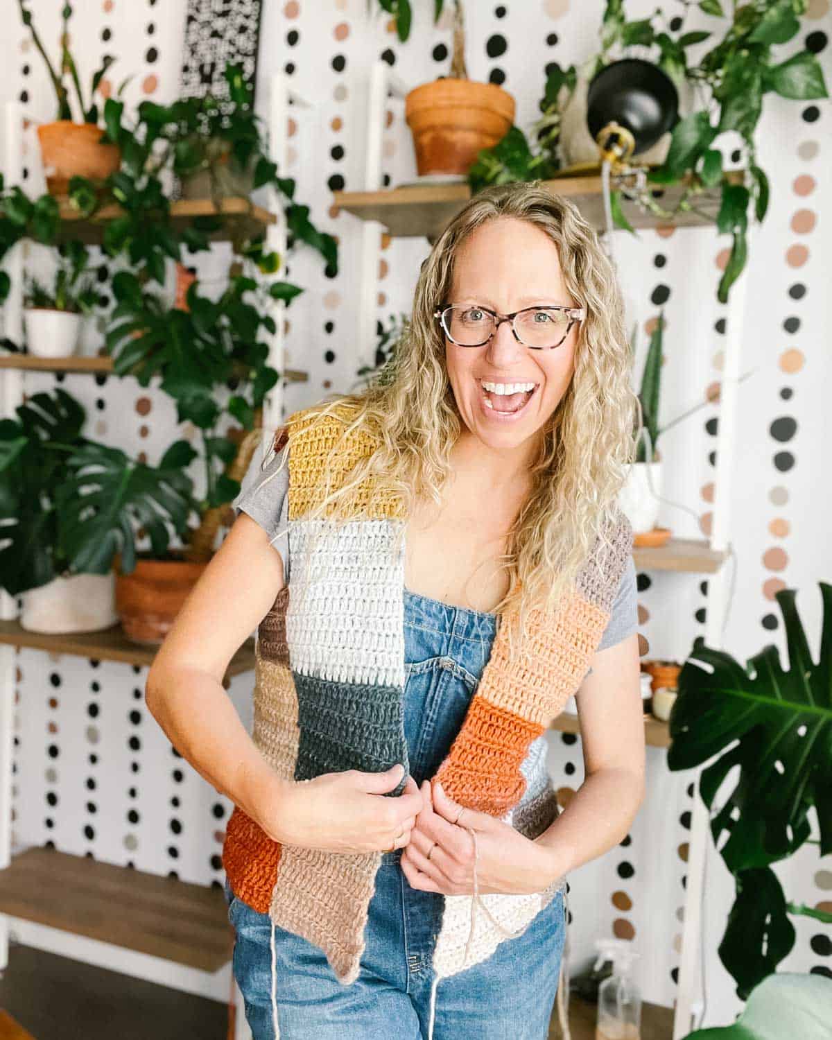 A blond woman with a large smile wearing a partially finished crochet patchwork sweater.