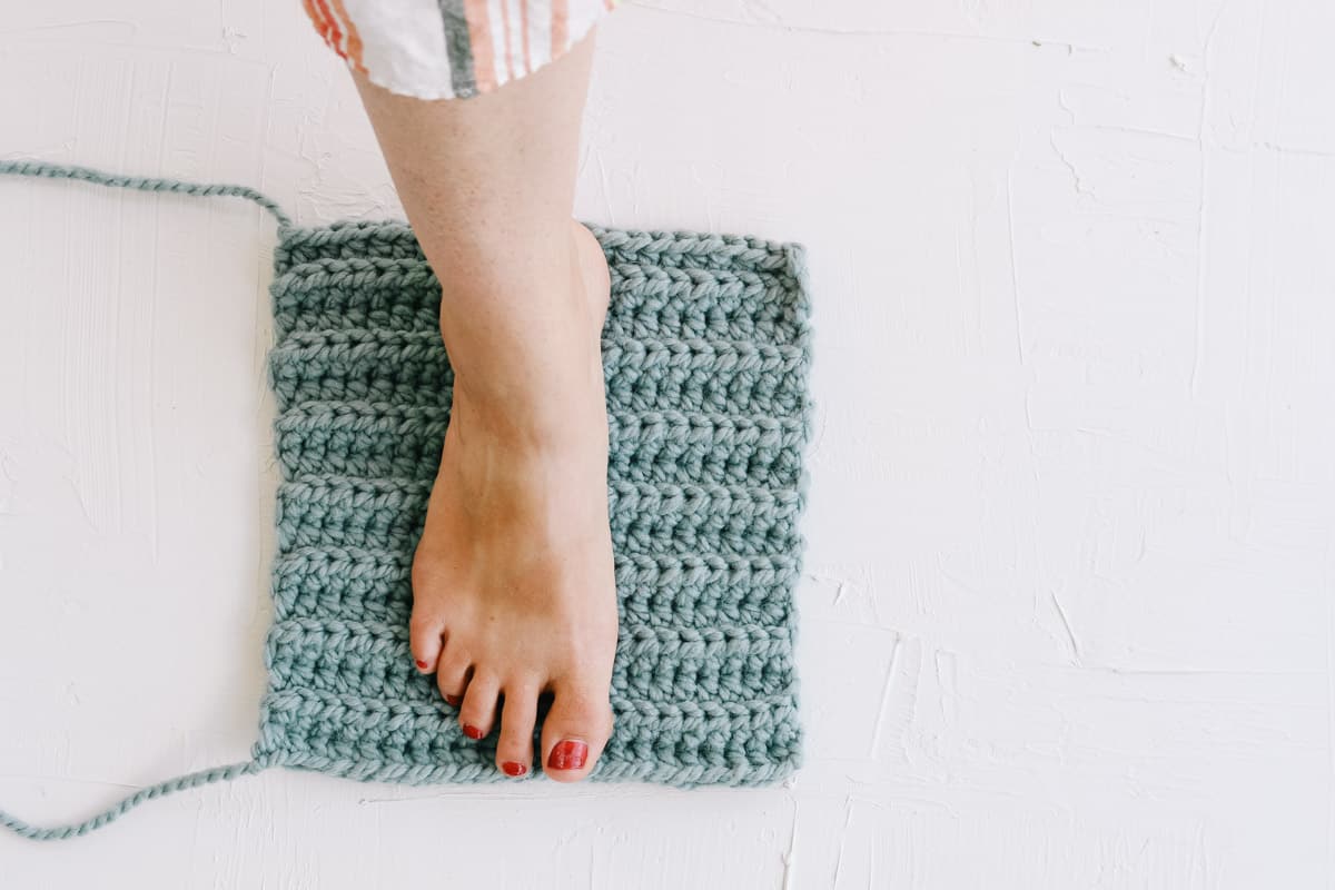 Woman's foot on a crochet rectangle as she creates simple crochet slippers.
