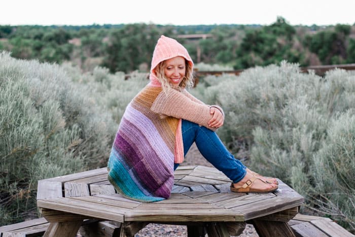 This rainbow gradient crochet cardigan includes pockets and a hood and is made with Lion Brand Mandala cake yarn.
