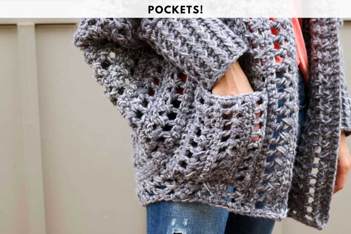 This image shows an up-close photo of a chunky gray crochet cardigan pocket. There is a hand in the pocket, displaying how deep the pocket is.
