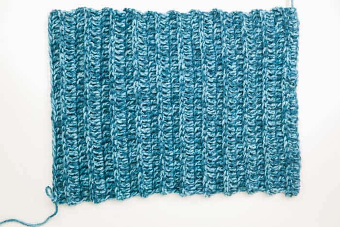 An overhead shot of a blue colored crochet rectangle on a white background.
