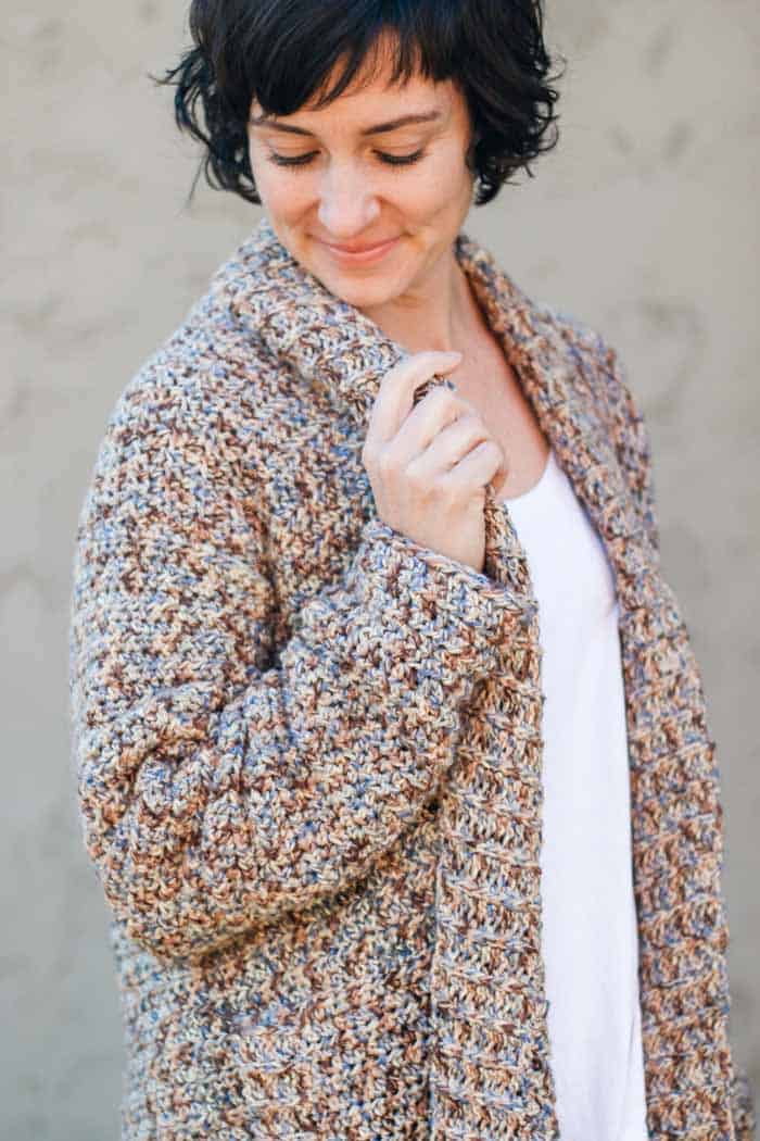 A woman looking down while holding the collar of a crochet one piece cardigan pattern.